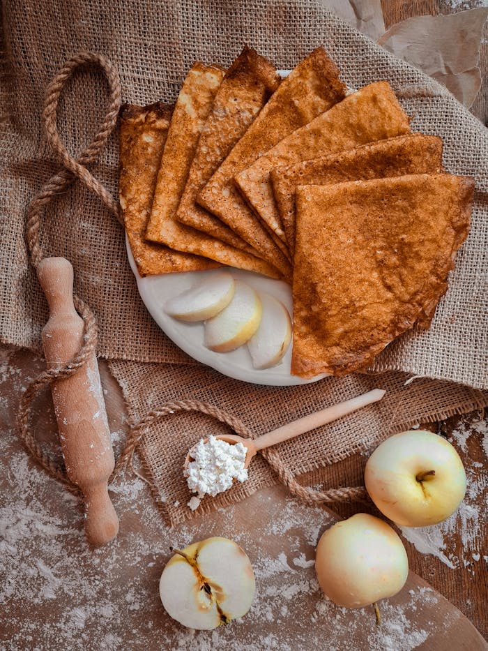 Flat lay of rustic crepes, fresh apples, and cottage cheese on burlap, perfect for autumn mood.